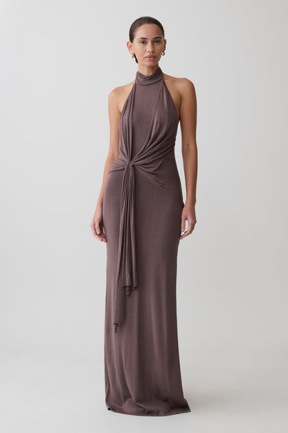 Woman wearing a long brown dress with a halter neck design on a white background